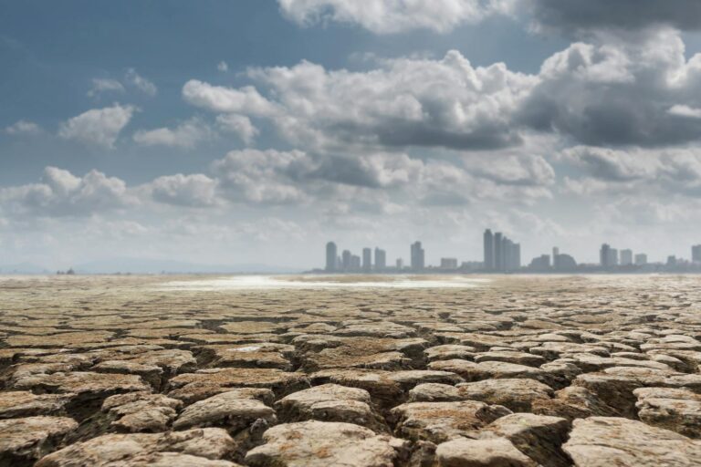 Vast territory of dried soil with contemporary buildings and skyscrapers on background on cloudy sunny day