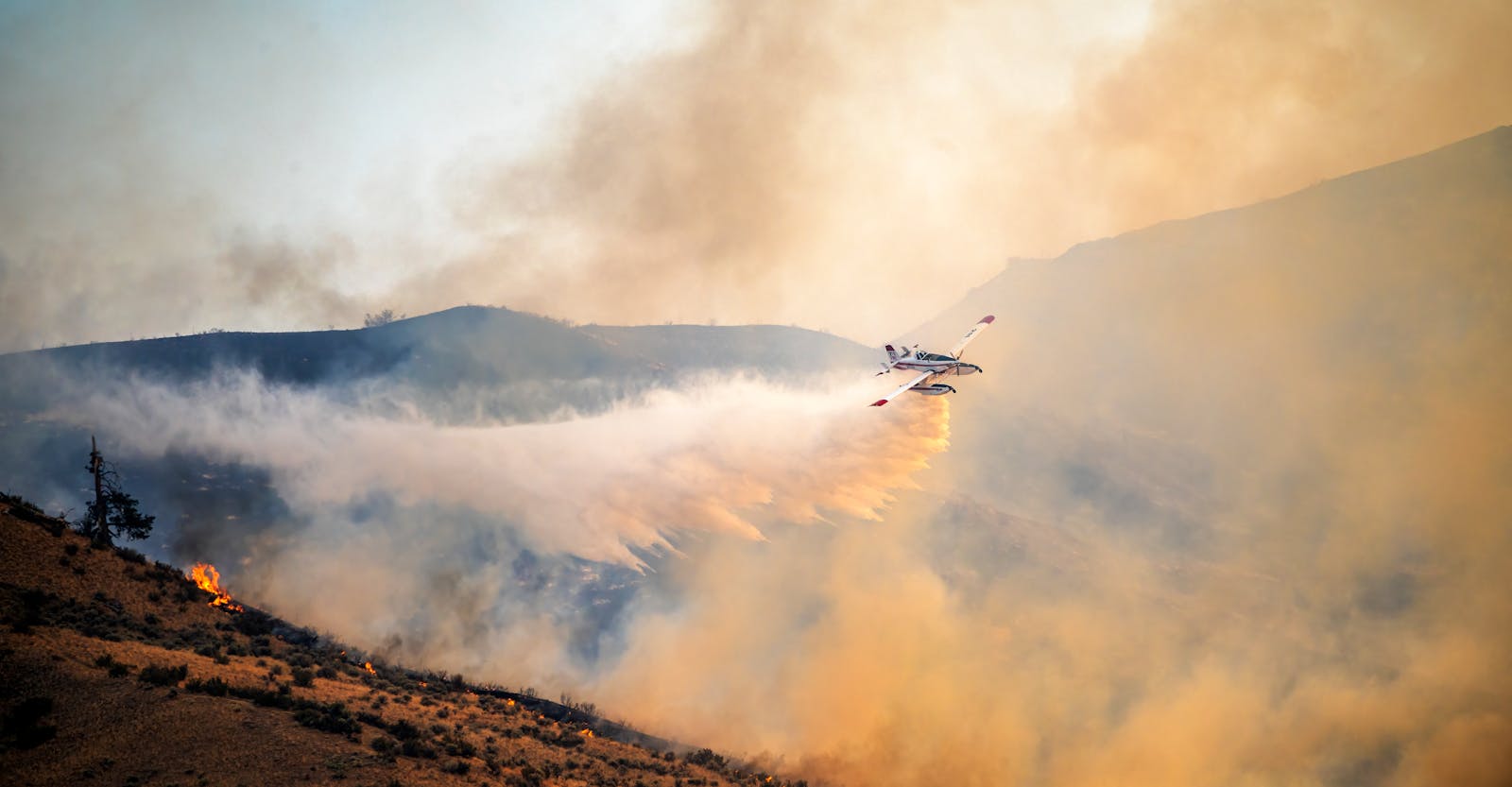 Airplane flying over burning hilly terrain and spreading extinguishing powder