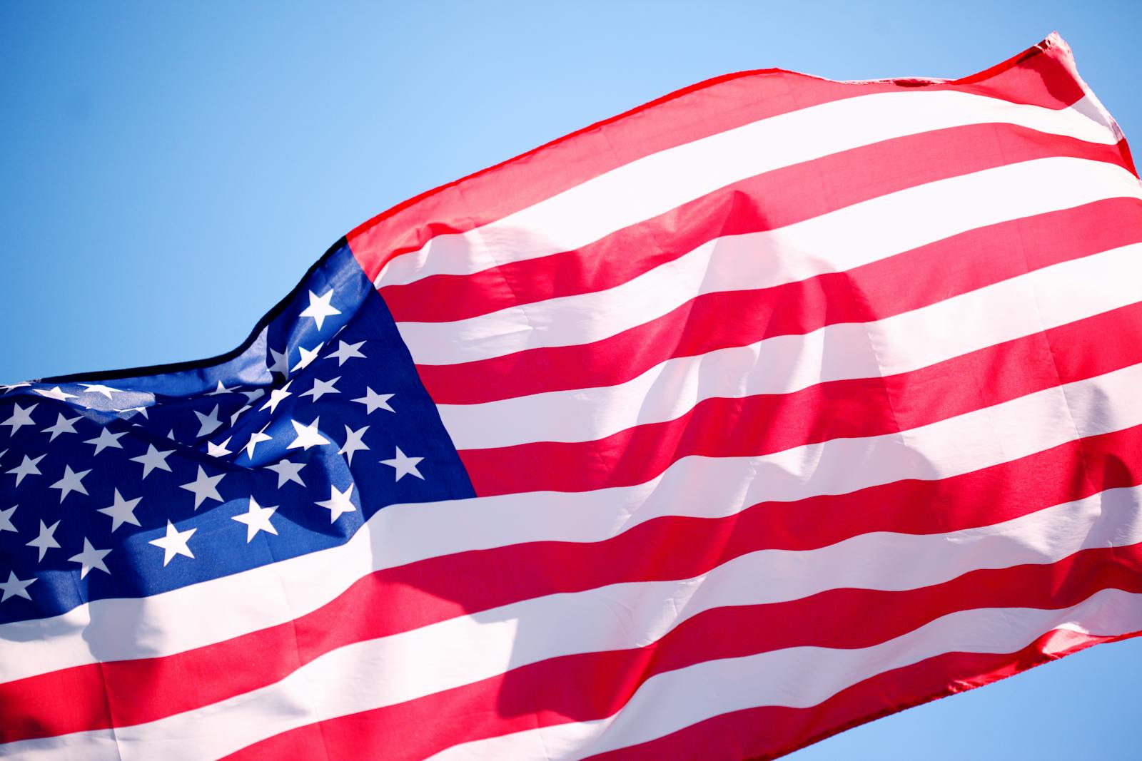 Close-up of the American flag waving in the wind against a clear blue sky.