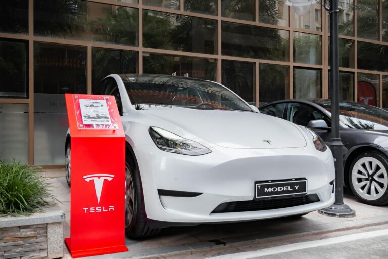 Tesla Model Y parked outdoors with a red display stand in front. Modern and sleek automotive design.