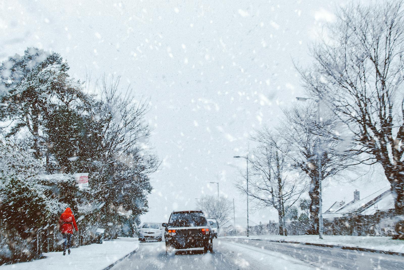 A car driving through a snowy road during a heavy winter storm, capturing a serene winter landscape.