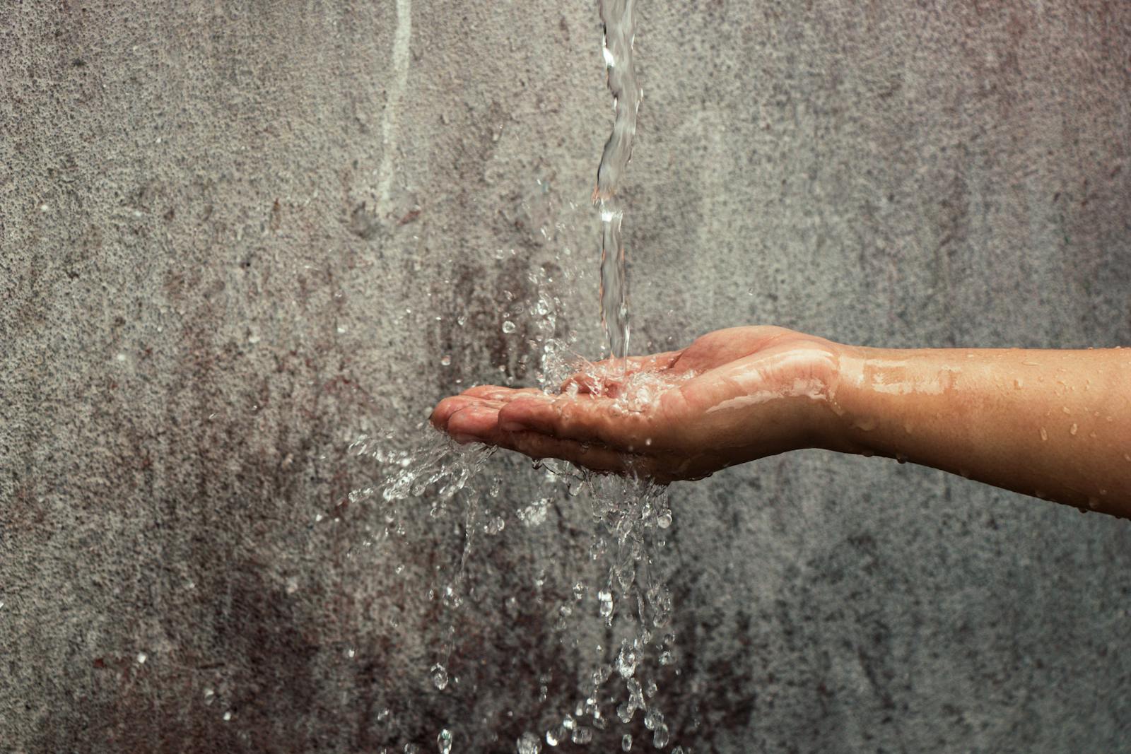 Hand catching a stream of water against a textured wall background.