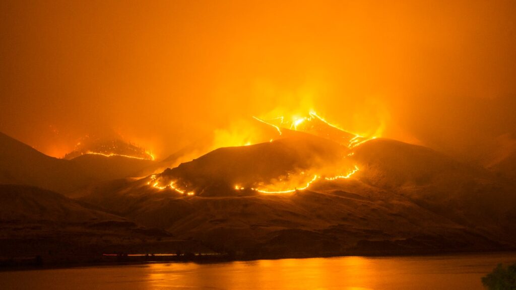 Intense wildfire blazing on hills, reflecting over a calm river in Orondo, Washington.