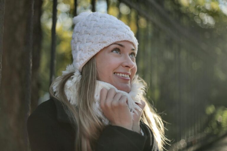 A joyful woman in a knit hat and scarf enjoying a sunny winter day outdoors.