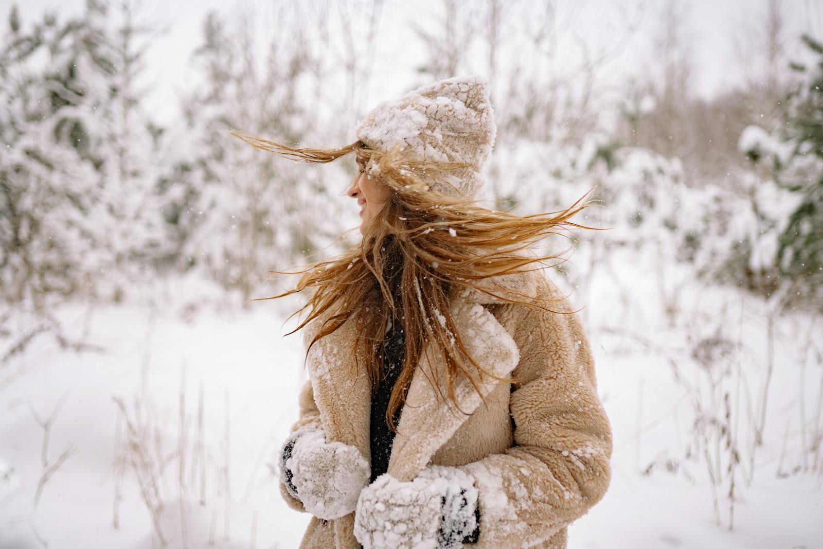 A woman smiles while enjoying a snowy winter day in a fur coat and beanie.